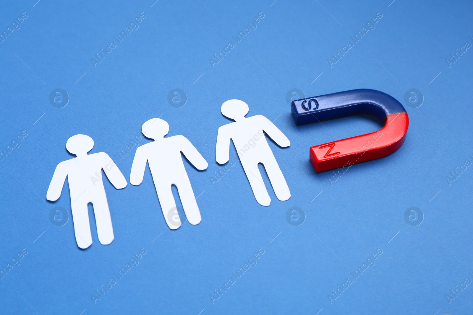 Photo of Magnet attracting paper human figures on blue background