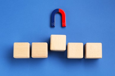 Photo of Magnet attracting wooden cubes on blue background, flat lay