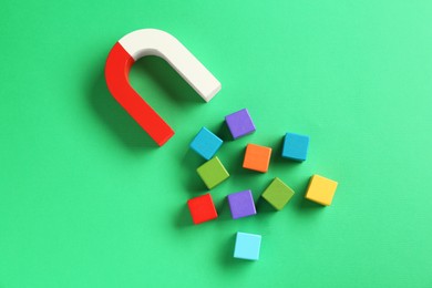 Photo of Magnet attracting colorful cubes on green background, flat lay