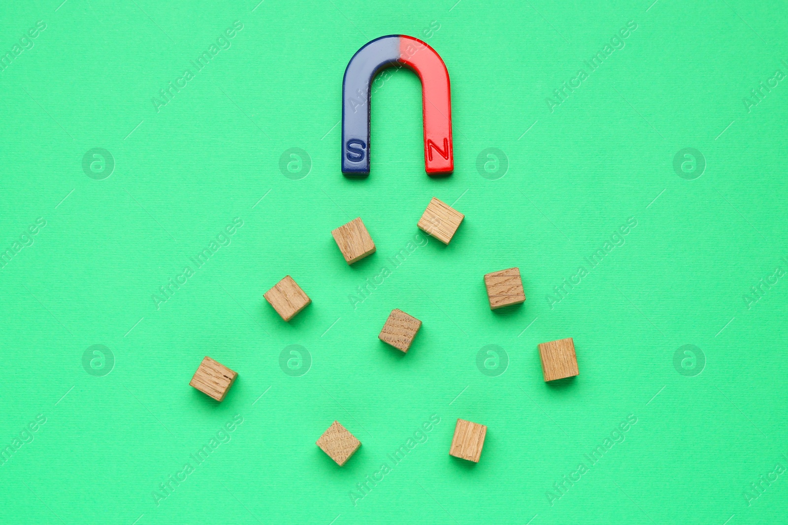 Photo of Magnet attracting wooden cubes on green background, flat lay