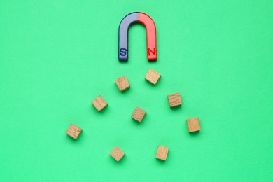 Photo of Magnet attracting wooden cubes on green background, flat lay