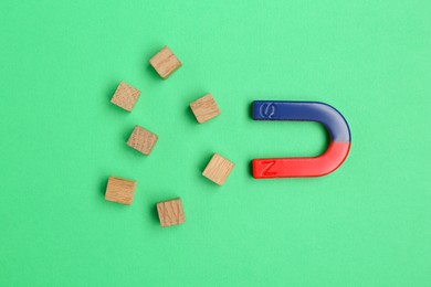 Photo of Magnet attracting wooden cubes on green background, flat lay