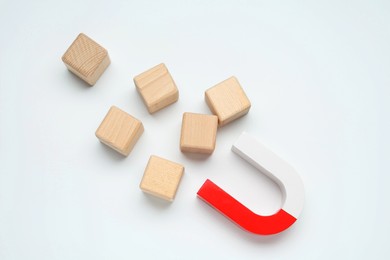 Photo of Magnet attracting wooden cubes on white background, flat lay