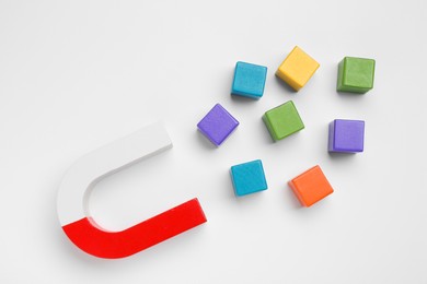 Photo of Magnet attracting colorful cubes on white background, flat lay