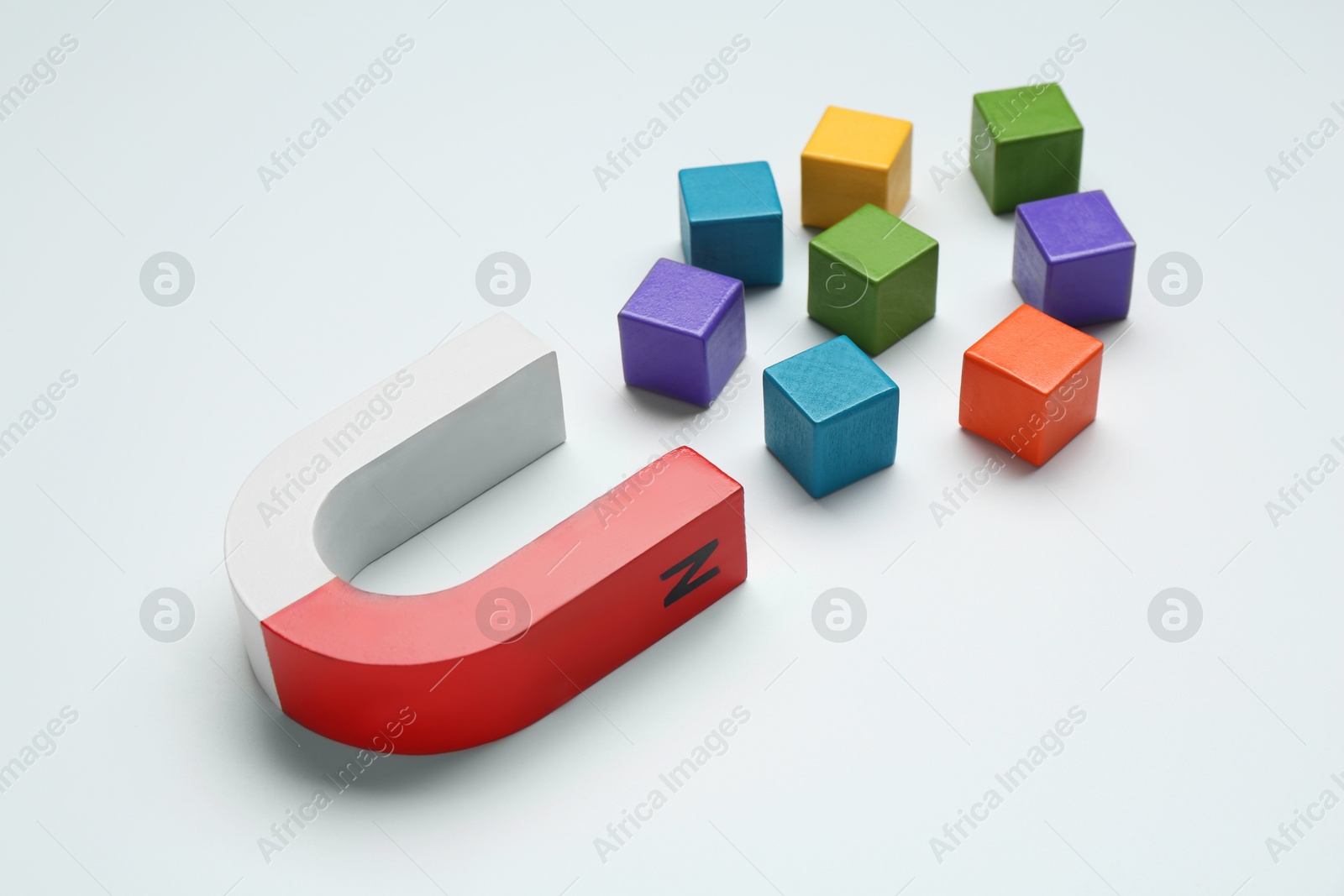 Photo of Magnet attracting colorful cubes on white background, closeup