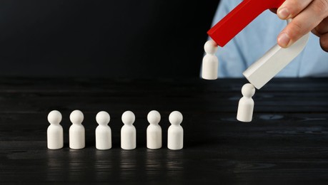 Photo of Man with magnet attracting human figures at black wooden table, closeup