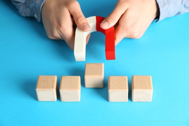 Photo of Man with magnet attracting wooden cubes on light blue background, closeup