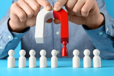 Photo of Man with magnet attracting red piece among wooden ones on light blue background, closeup