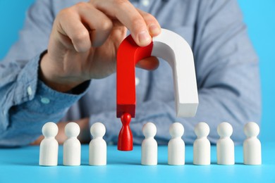 Photo of Man with magnet attracting red piece among wooden ones on light blue background, closeup