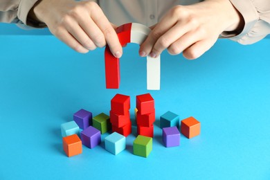 Photo of Woman with magnet attracting colorful cubes on light blue background, closeup