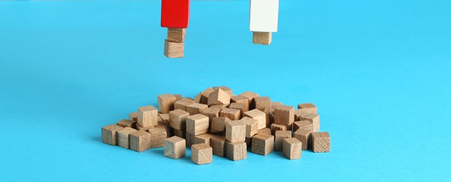 Photo of Magnet attracting wooden cubes on light blue background, closeup