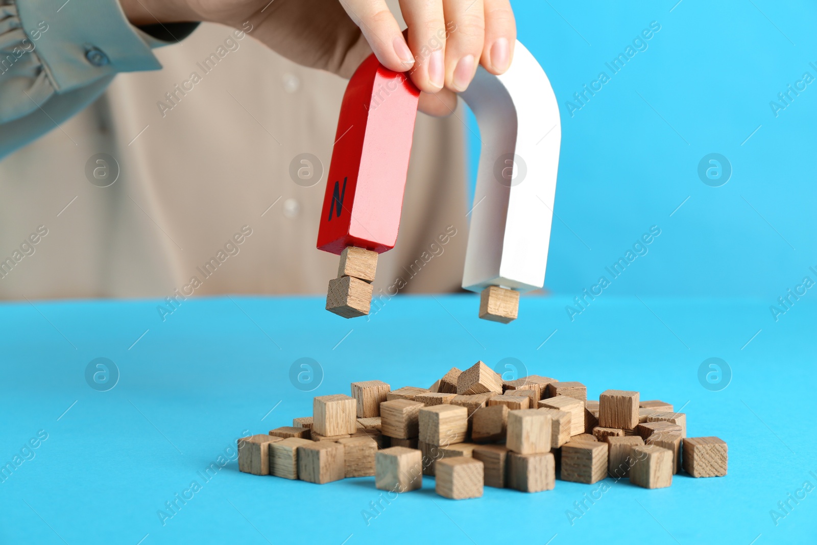 Photo of Woman with magnet attracting wooden cubes on light blue background, closeup