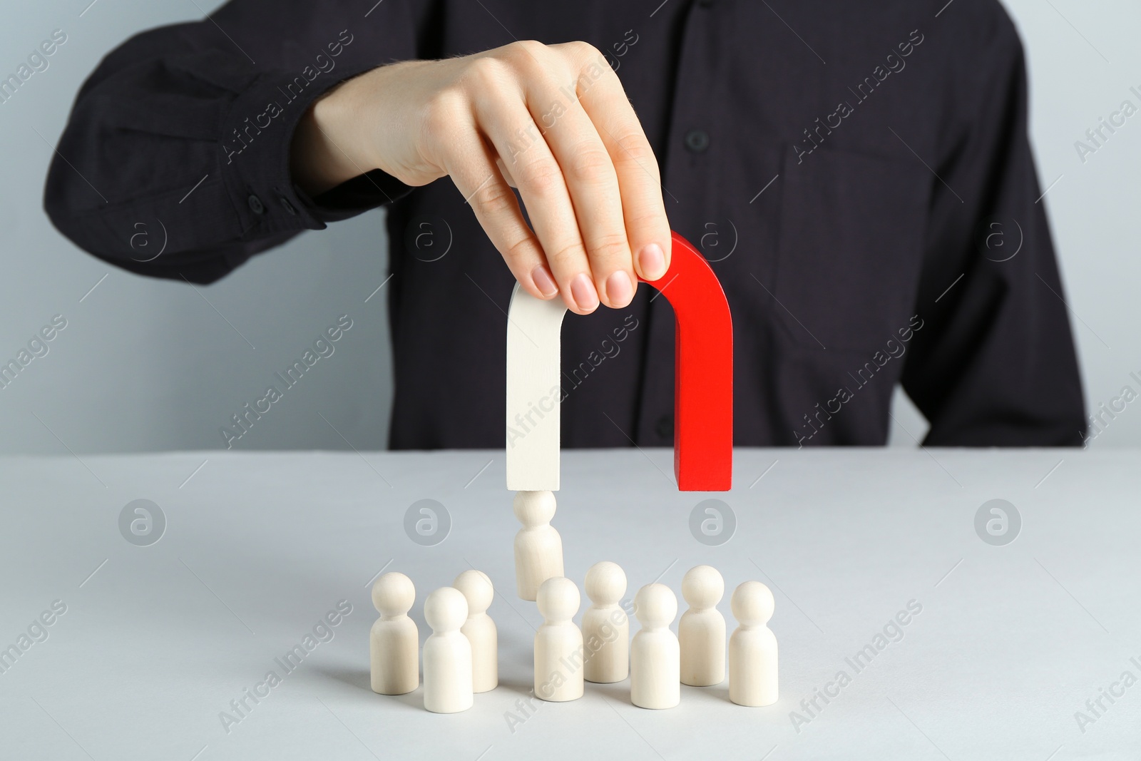 Photo of Woman with magnet attracting piece among wooden ones at white table, closeup