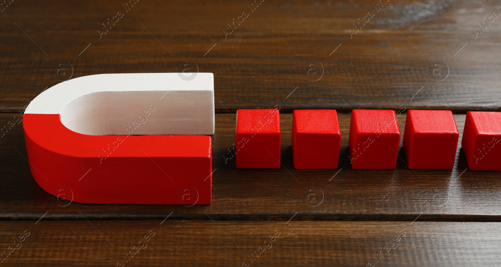 Photo of Magnet attracting red cubes on wooden table, closeup