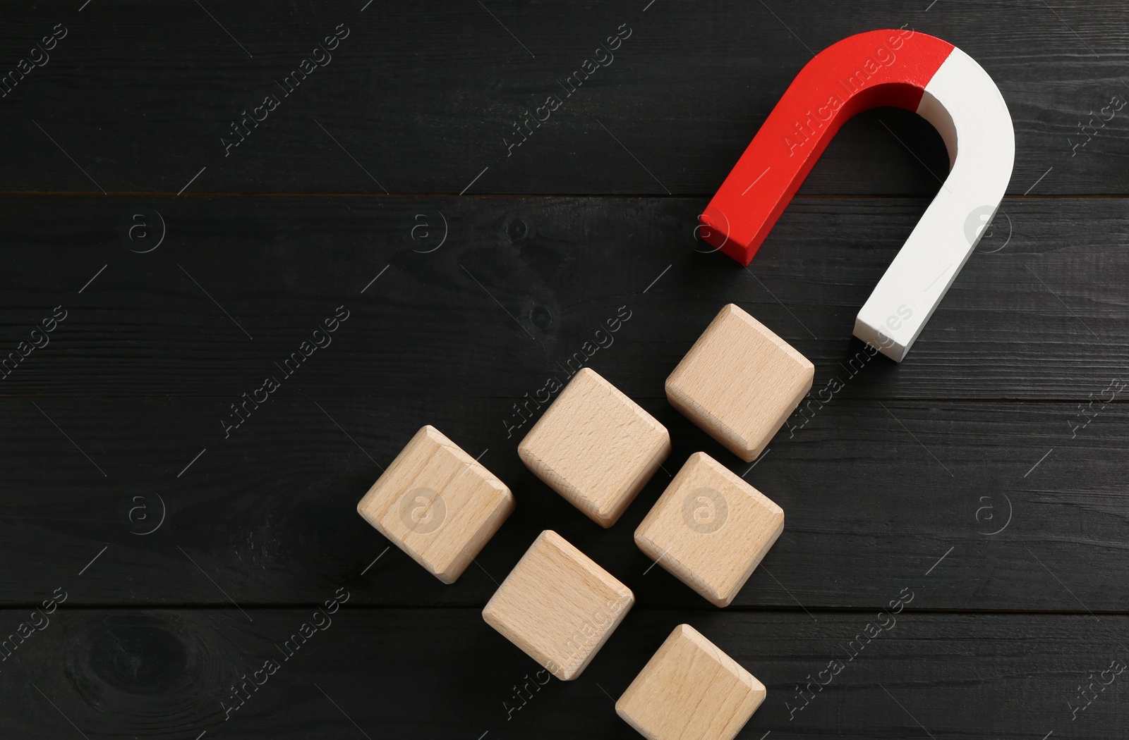 Photo of Magnet attracting cubes on black wooden table, flat lay. Space for text