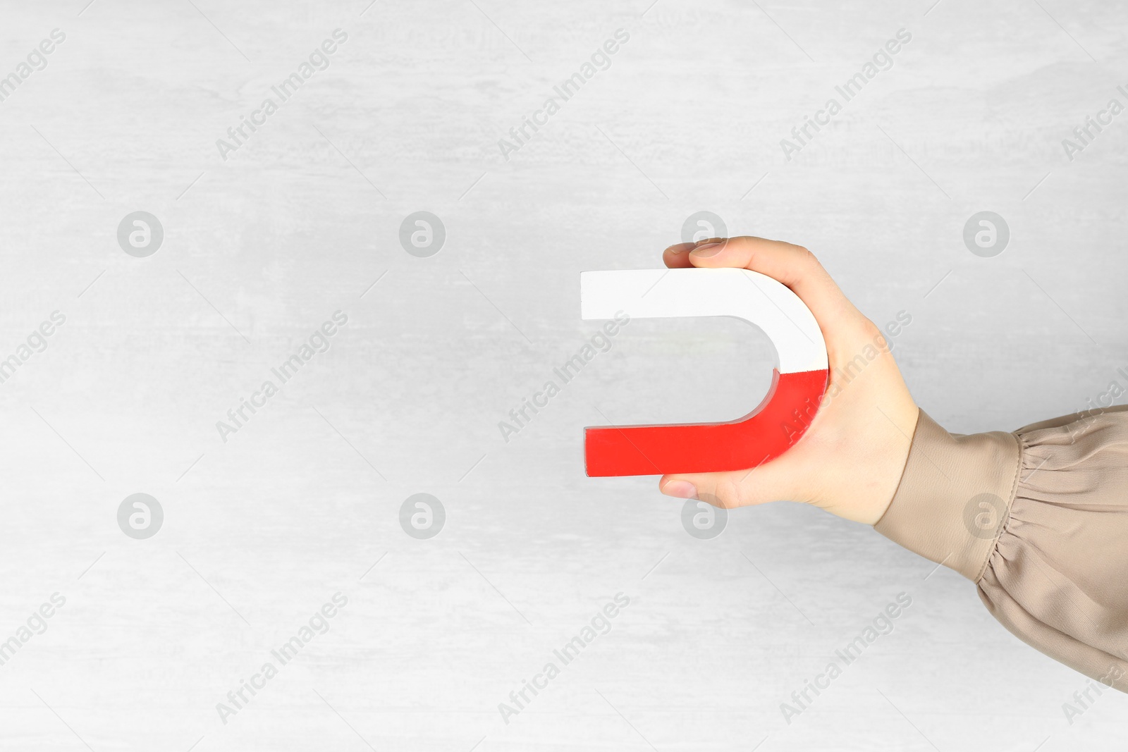 Photo of Woman with horseshoe magnet on light background, closeup. Space for text