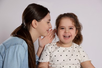 Photo of Teenage girl whispering secret to her cute little sister on white background