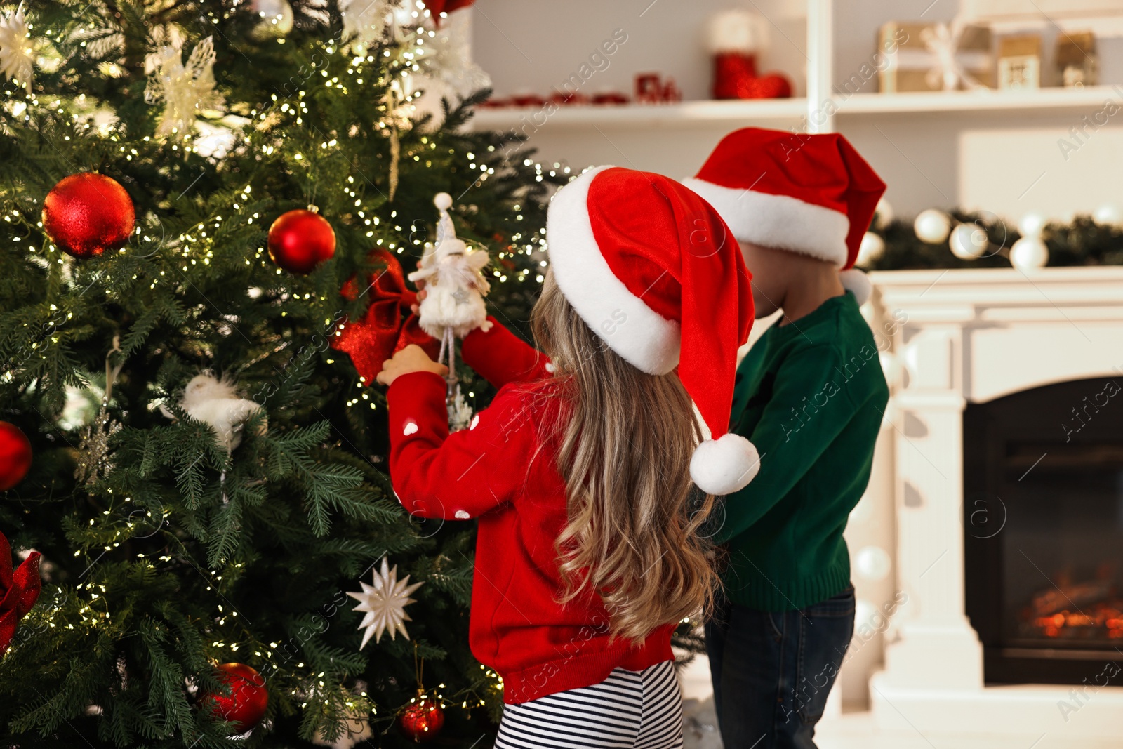 Photo of Little kids in Santa hats decorating Christmas tree at home