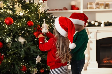 Little kids in Santa hats decorating Christmas tree at home