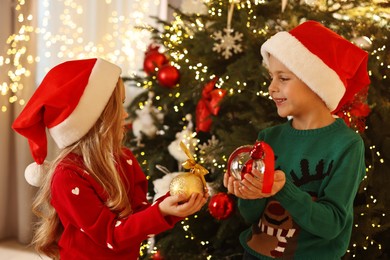 Little kids in Santa hats with Christmas ornaments at home