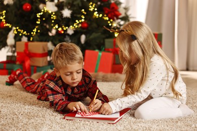 Little kids writing letter to Santa Claus on floor at home. Christmas celebration