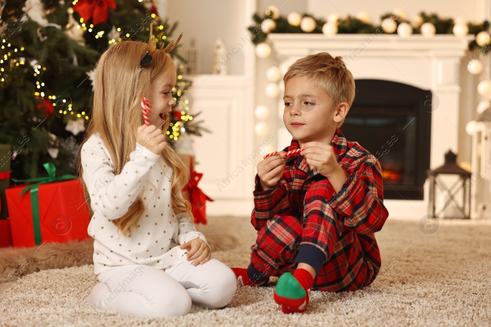 Photo of Little kids with candy canes on floor at home. Christmas celebration