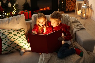 Photo of Little kids reading book on sofa at home. Christmas celebration