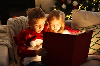 Photo of Little kids reading book on sofa at home. Christmas celebration