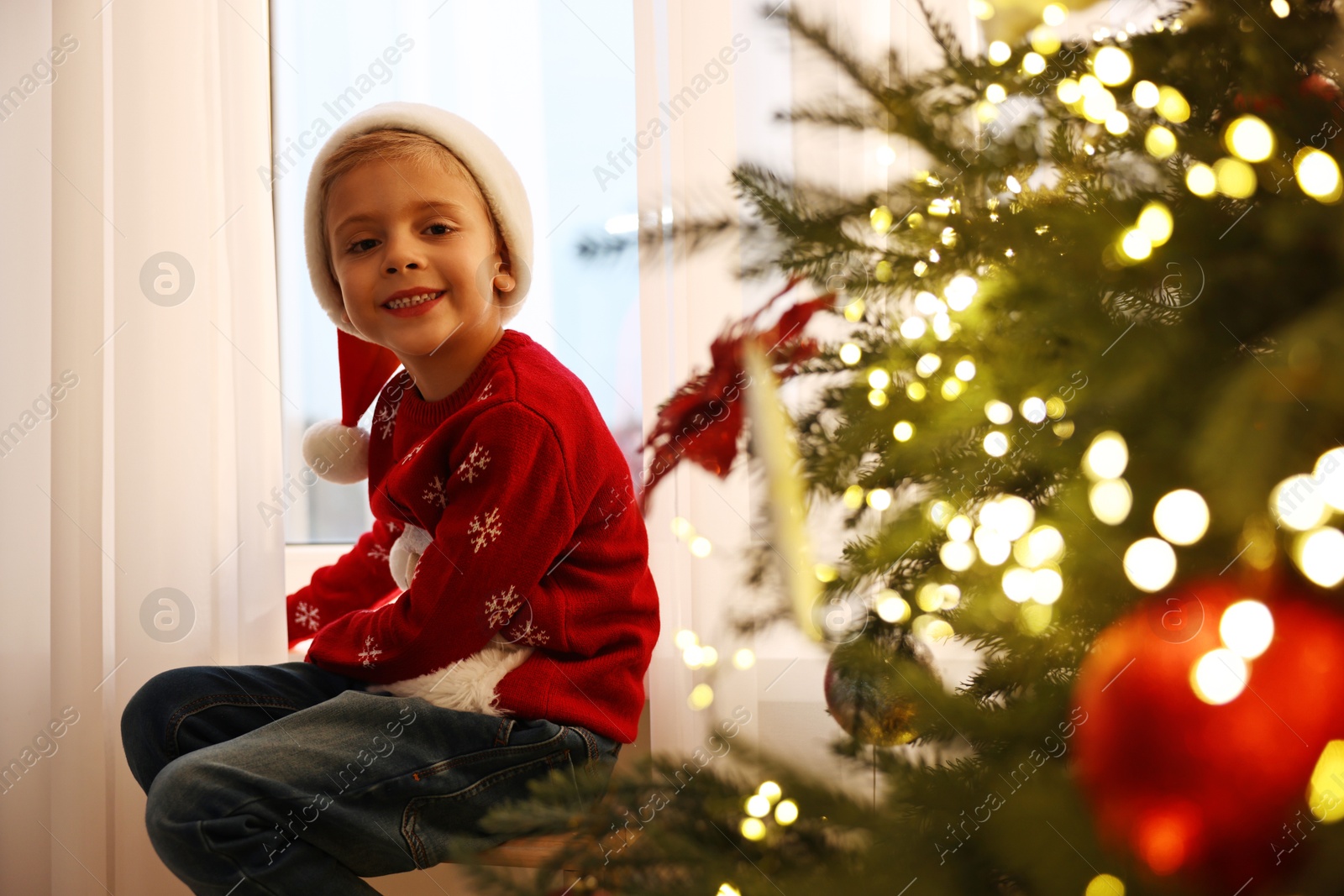 Photo of Little boy with Santa hat near window in room decorated for Christmas