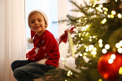 Photo of Little boy with Santa hat near window in room decorated for Christmas