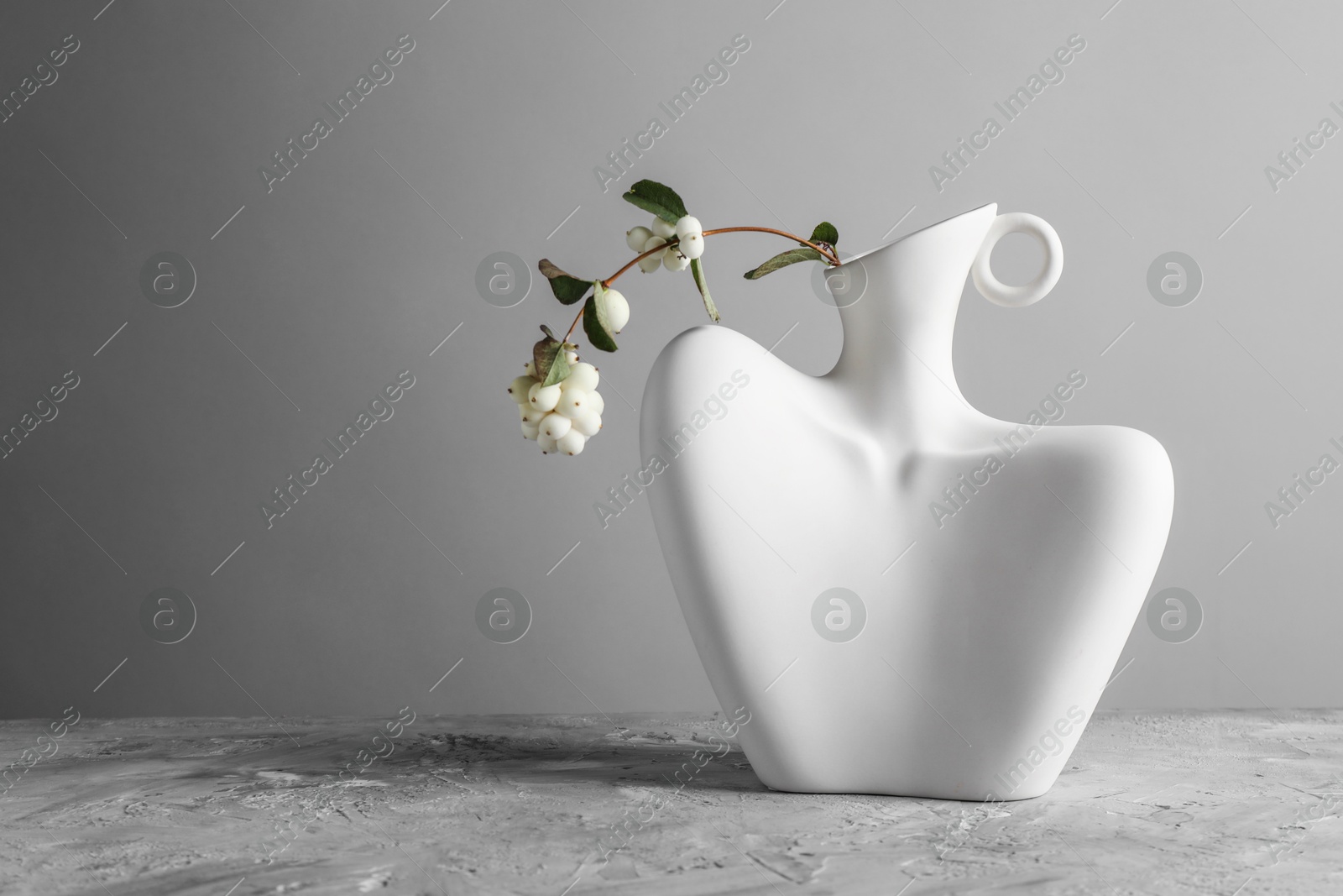 Photo of Stylish vase with snowberry branch on grey table, space for text