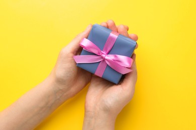 Photo of Woman holding gift box with pink bow on yellow background, top view