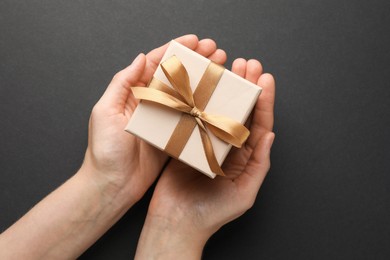 Photo of Woman holding gift box with golden bow on black background, top view