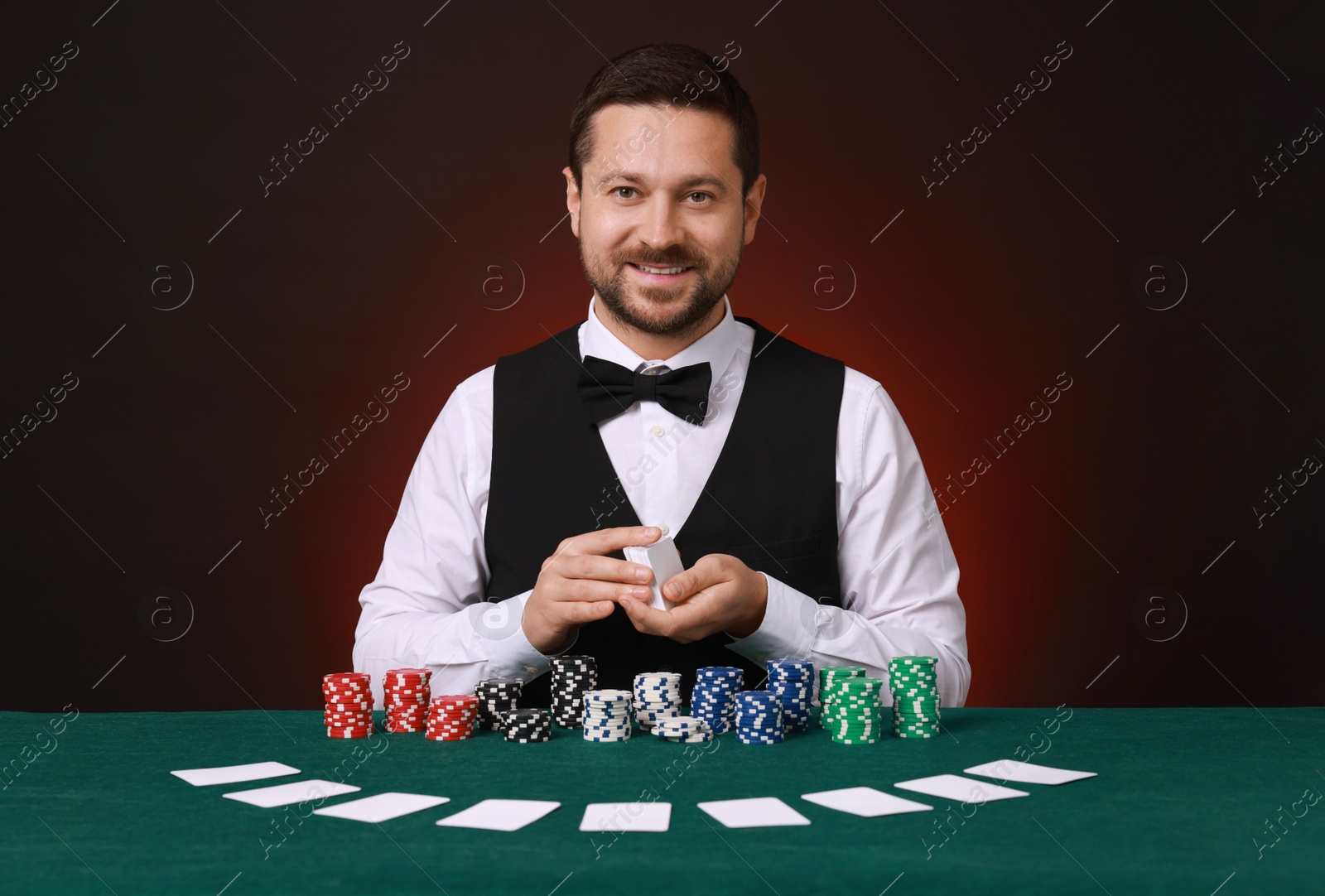 Photo of Professional croupier shuffling cards at gambling table against dark red background