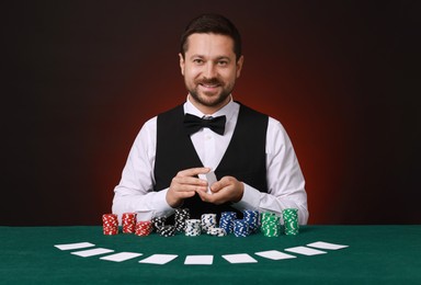 Photo of Professional croupier shuffling cards at gambling table against dark red background