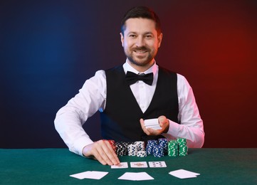 Photo of Professional croupier with playing cards at gambling table against color background