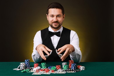 Photo of Professional croupier shuffling cards at gambling table against dark yellow background