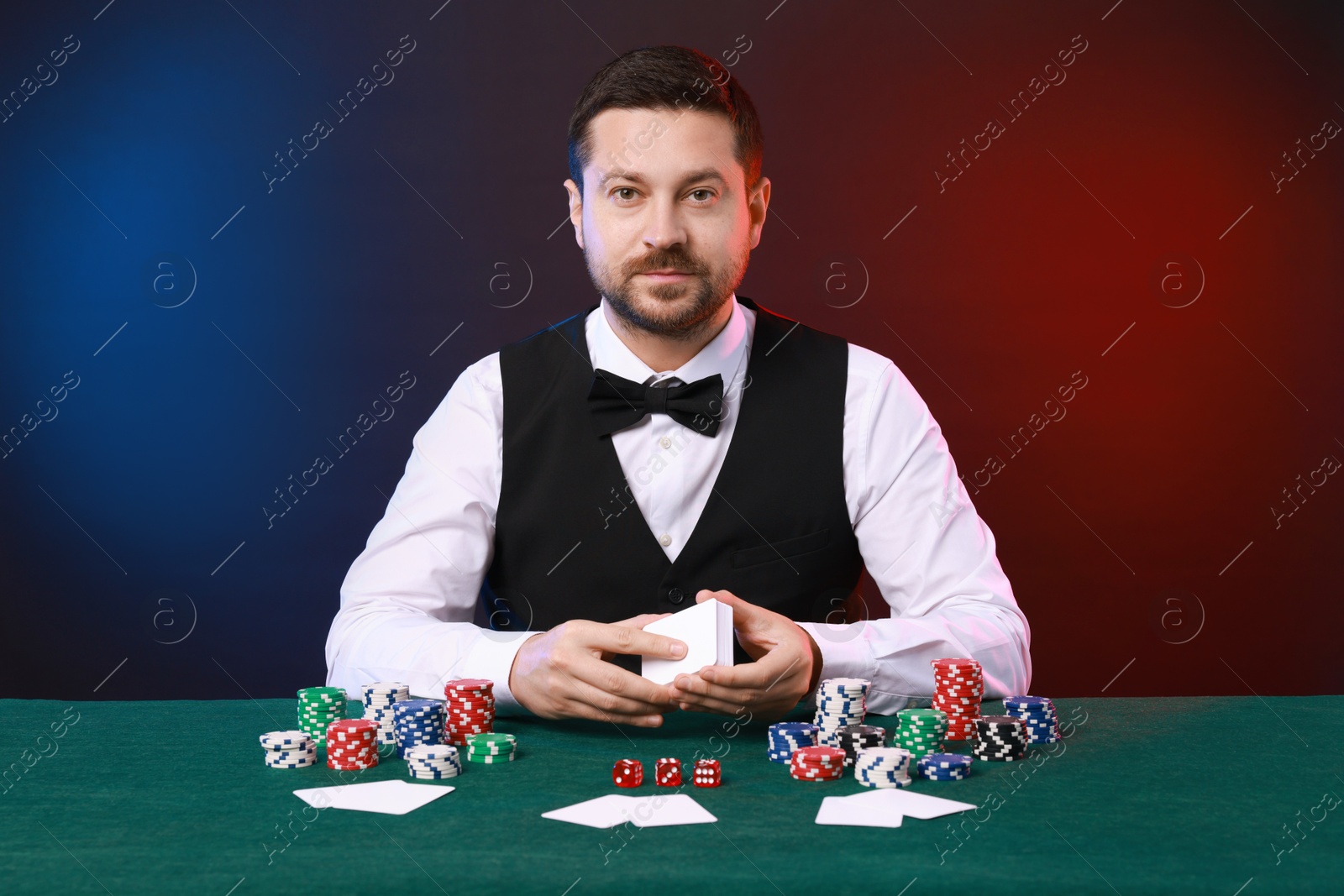 Photo of Professional croupier with playing cards at gambling table against color background