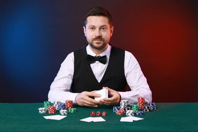 Photo of Professional croupier with playing cards at gambling table against color background