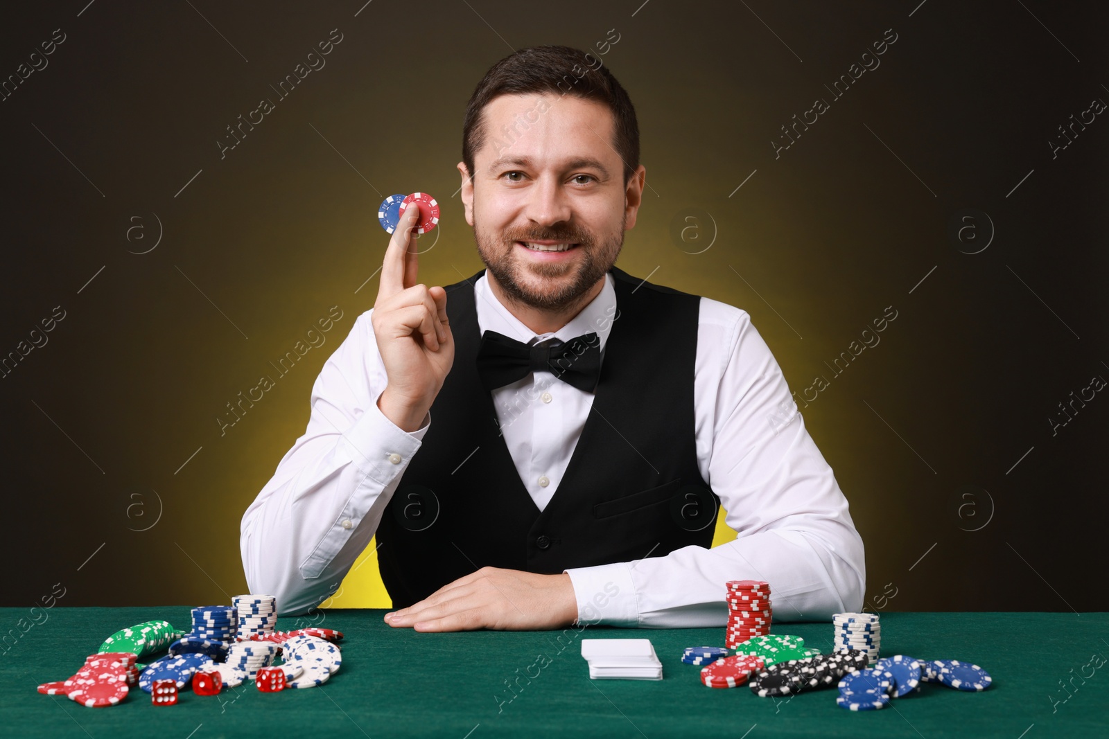 Photo of Professional croupier with casino chips at gambling table on dark yellow background