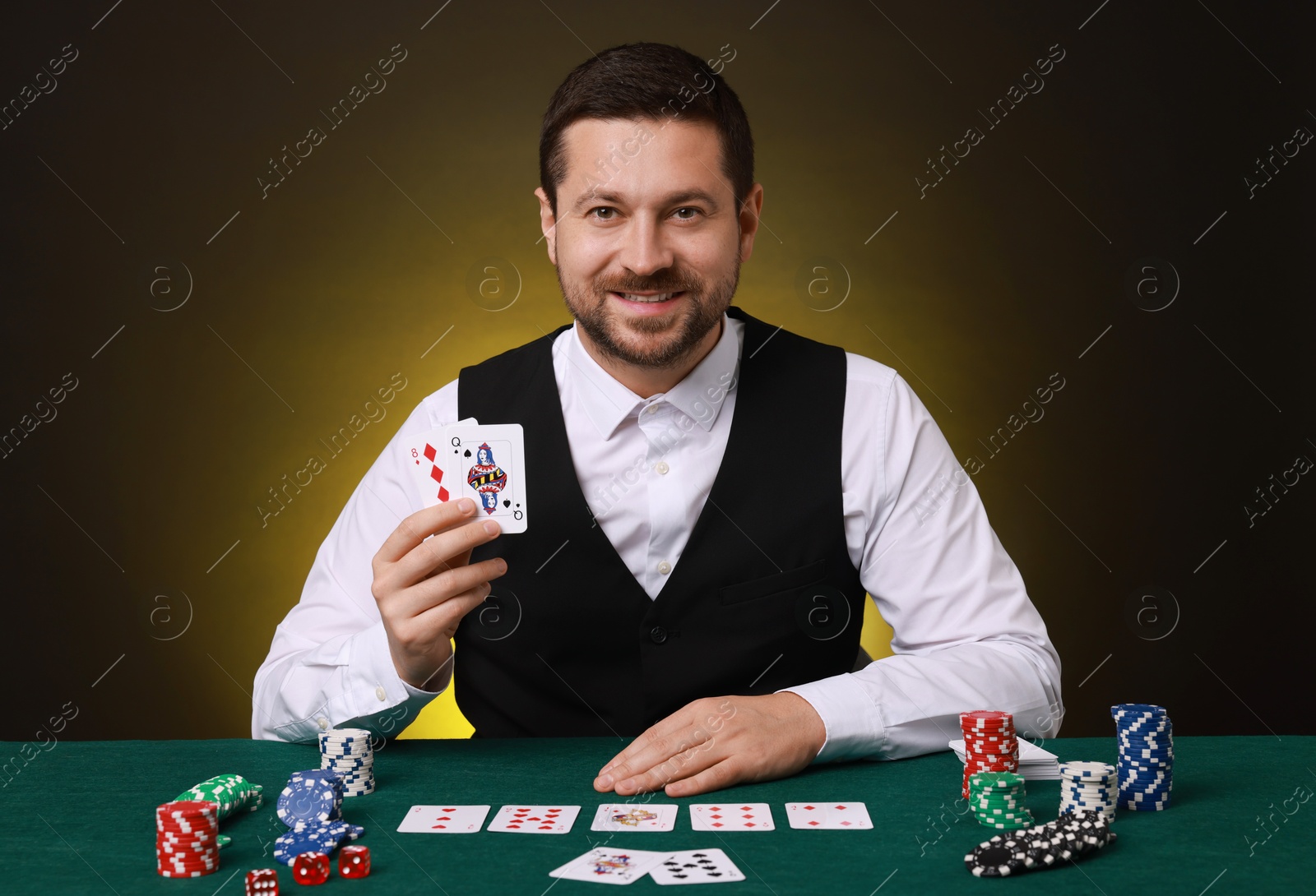 Photo of Professional croupier with playing cards at gambling table on dark yellow background