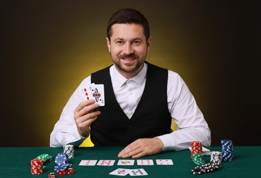 Photo of Professional croupier with playing cards at gambling table on dark yellow background