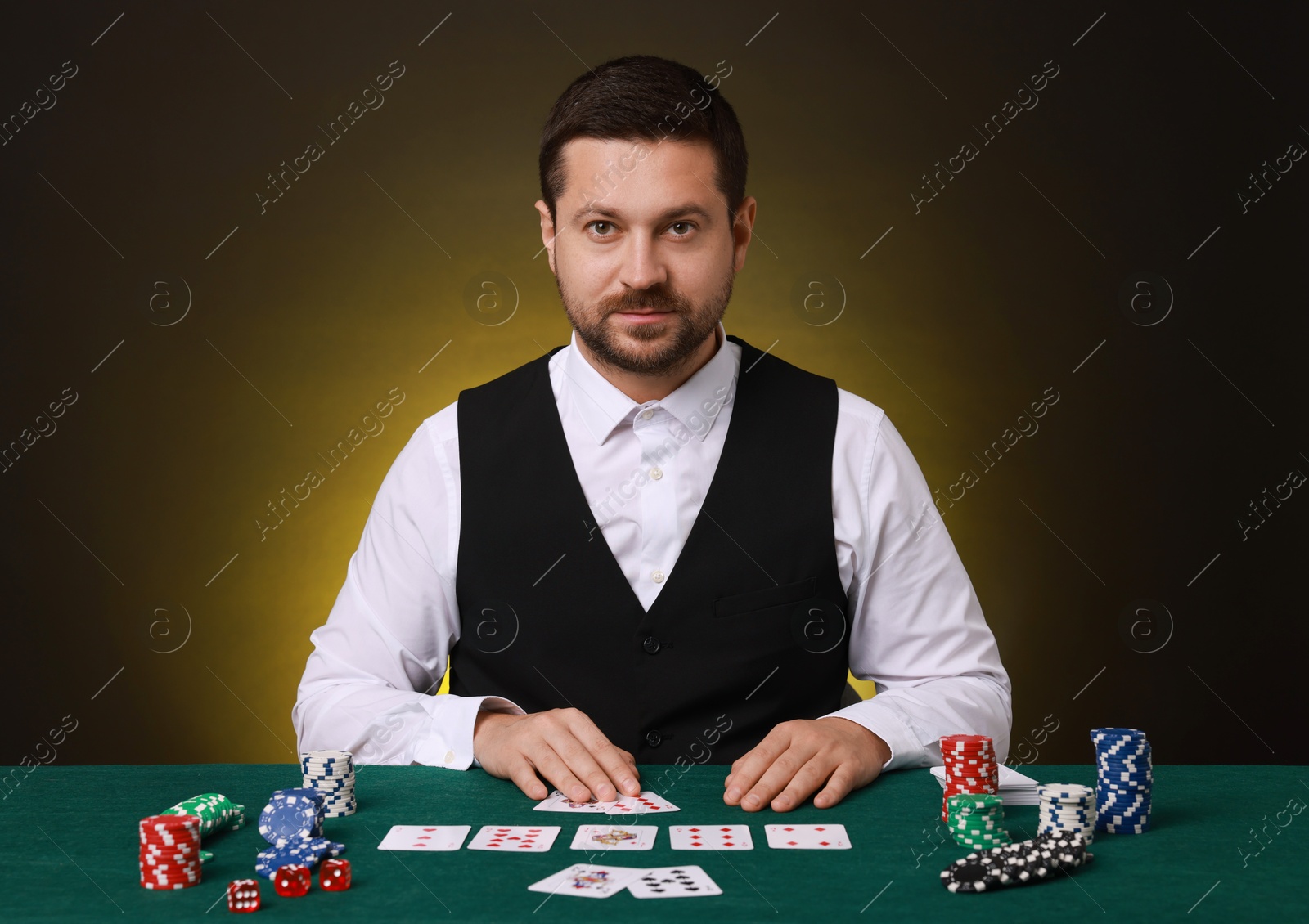 Photo of Professional croupier with playing cards at gambling table on dark yellow background