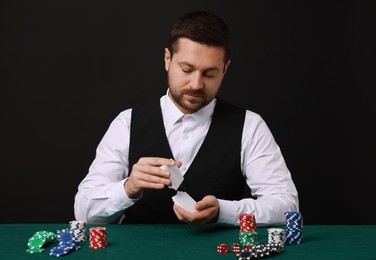 Photo of Professional croupier shuffling cards at gambling table against black background