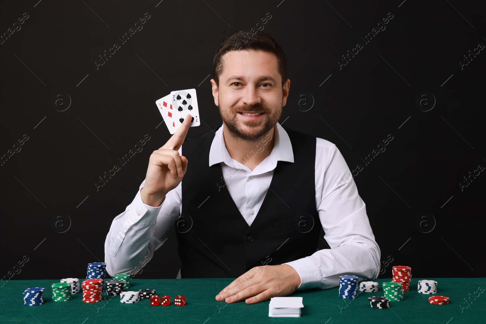 Photo of Professional croupier with playing cards at gambling table against black background