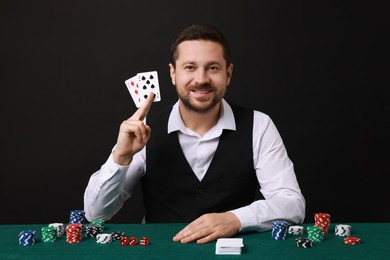 Photo of Professional croupier with playing cards at gambling table against black background