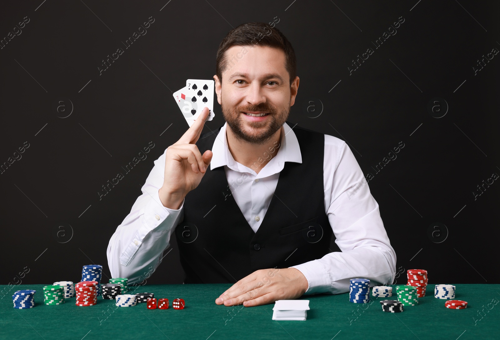 Photo of Professional croupier with playing cards at gambling table against black background