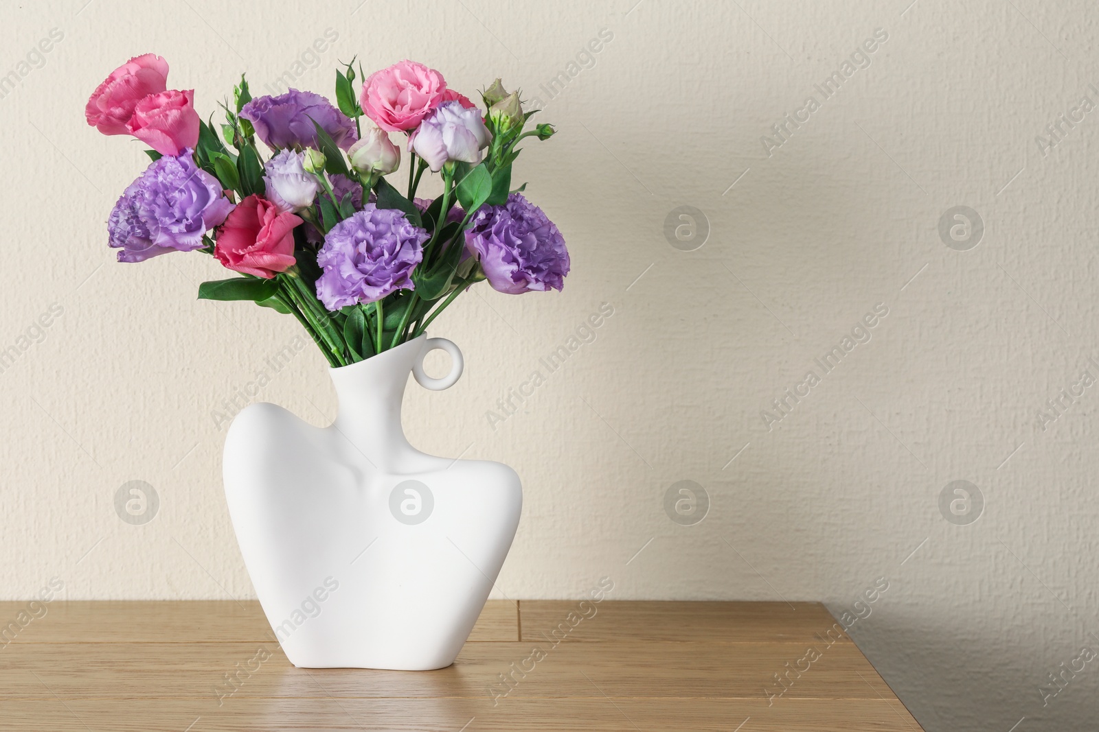 Photo of Vase with beautiful eustoma flowers on wooden table, space for text