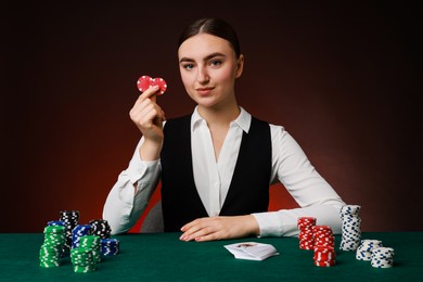 Photo of Professional croupier with casino chips and playing cards at gambling table on color background