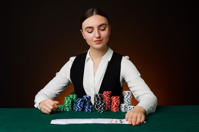 Photo of Professional croupier with casino chips and playing cards at gambling table on color background